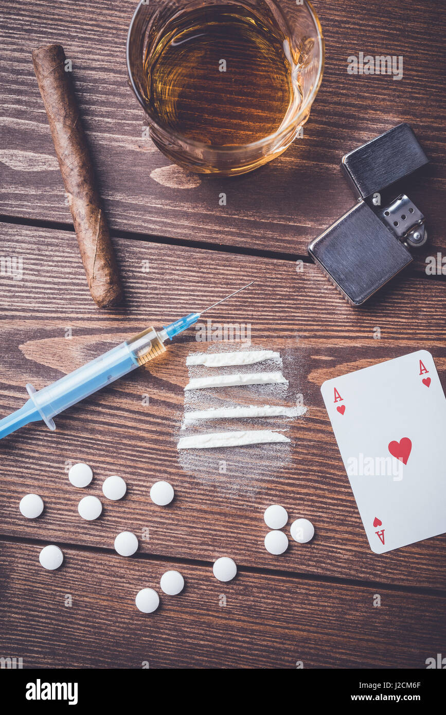 Droghe pesanti con le pillole, giocando a carte, siringa e alcool sul tavolo di legno Foto Stock