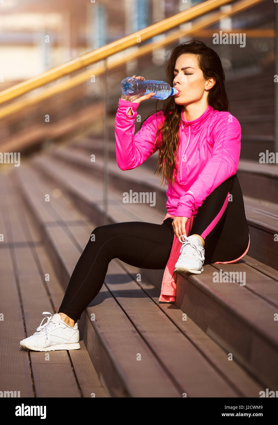 Giovane bella donna fit in appoggio su scale e bere acqua dopo il suo esercizio. Foto Stock