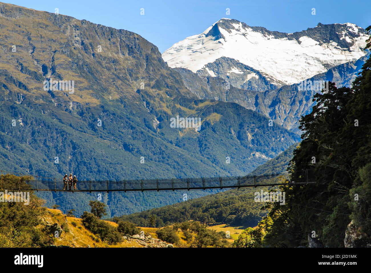 Gli escursionisti attraversare un ponte pedonale sopra il fiume Matukituki su Rob Roy Sentiero del ghiacciaio al di fuori di Wanaka, Nuova Zelanda. Foto Stock