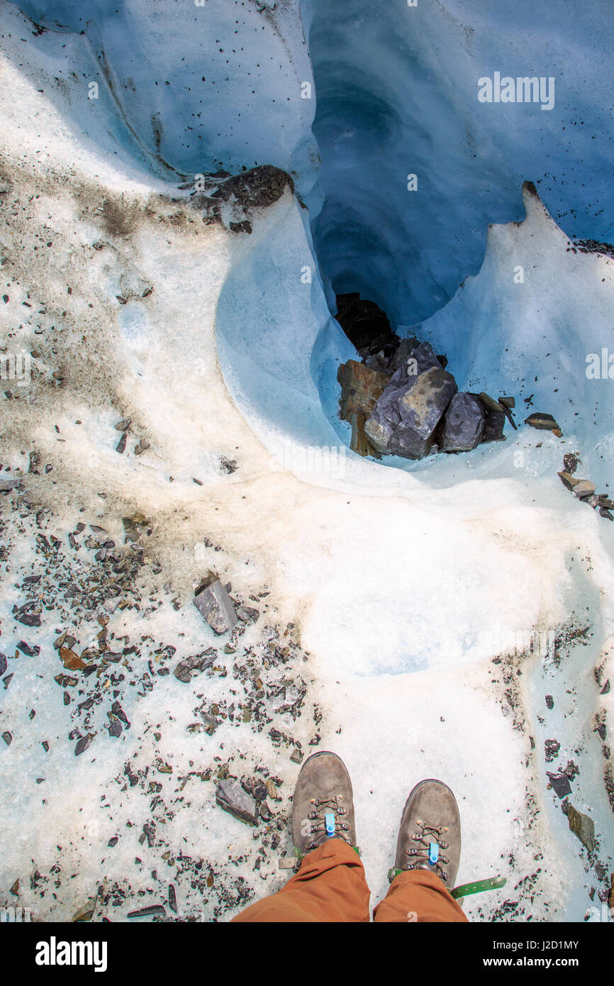 Guardando verso il basso in un crepaccio sul ghiacciaio Fox con escursionista piedi in primo piano. Foto Stock