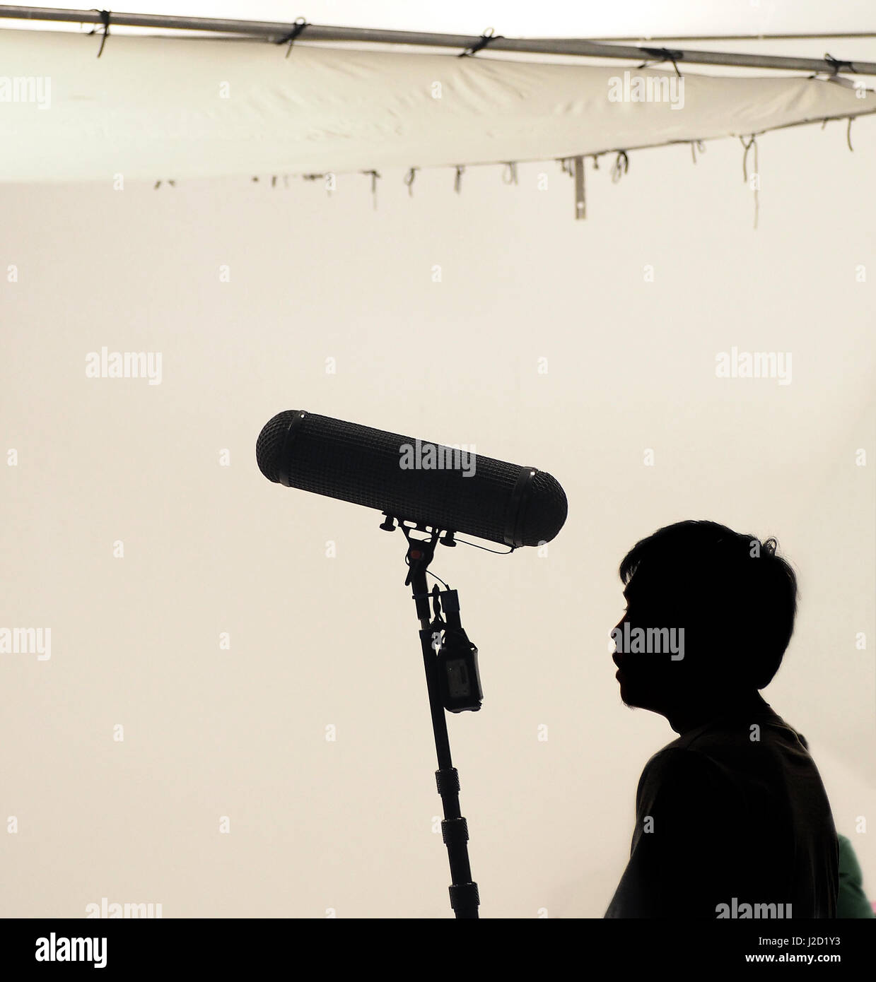 Microfono boom tenere premuto fino ad alta mediante video o film di produzione equipaggio del team uomo e la registrazione audio di un filmato in un grande studio. Foto Stock