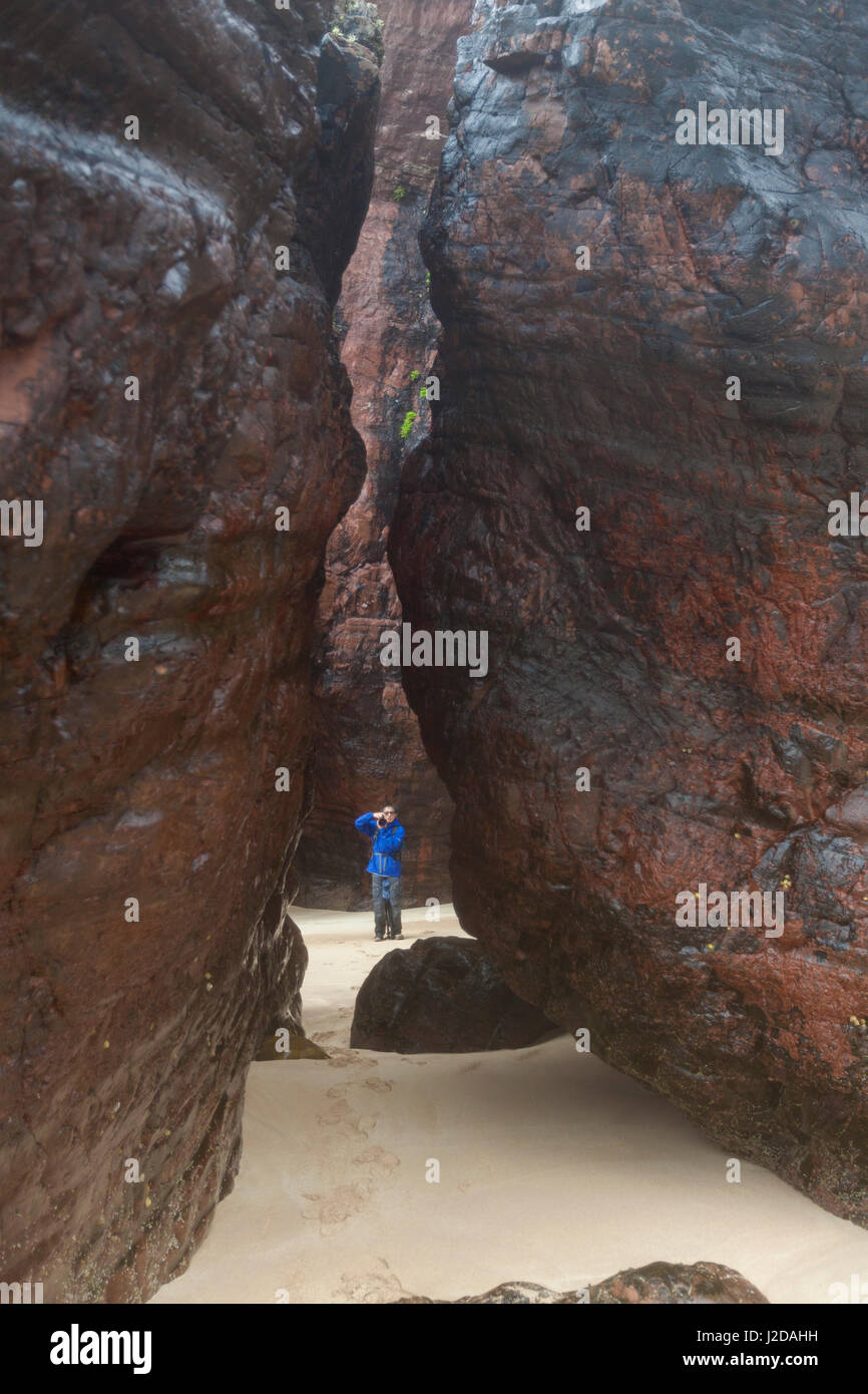 Fotografo di scattare le foto tra due grandi rocce sulla spiaggia Foto Stock