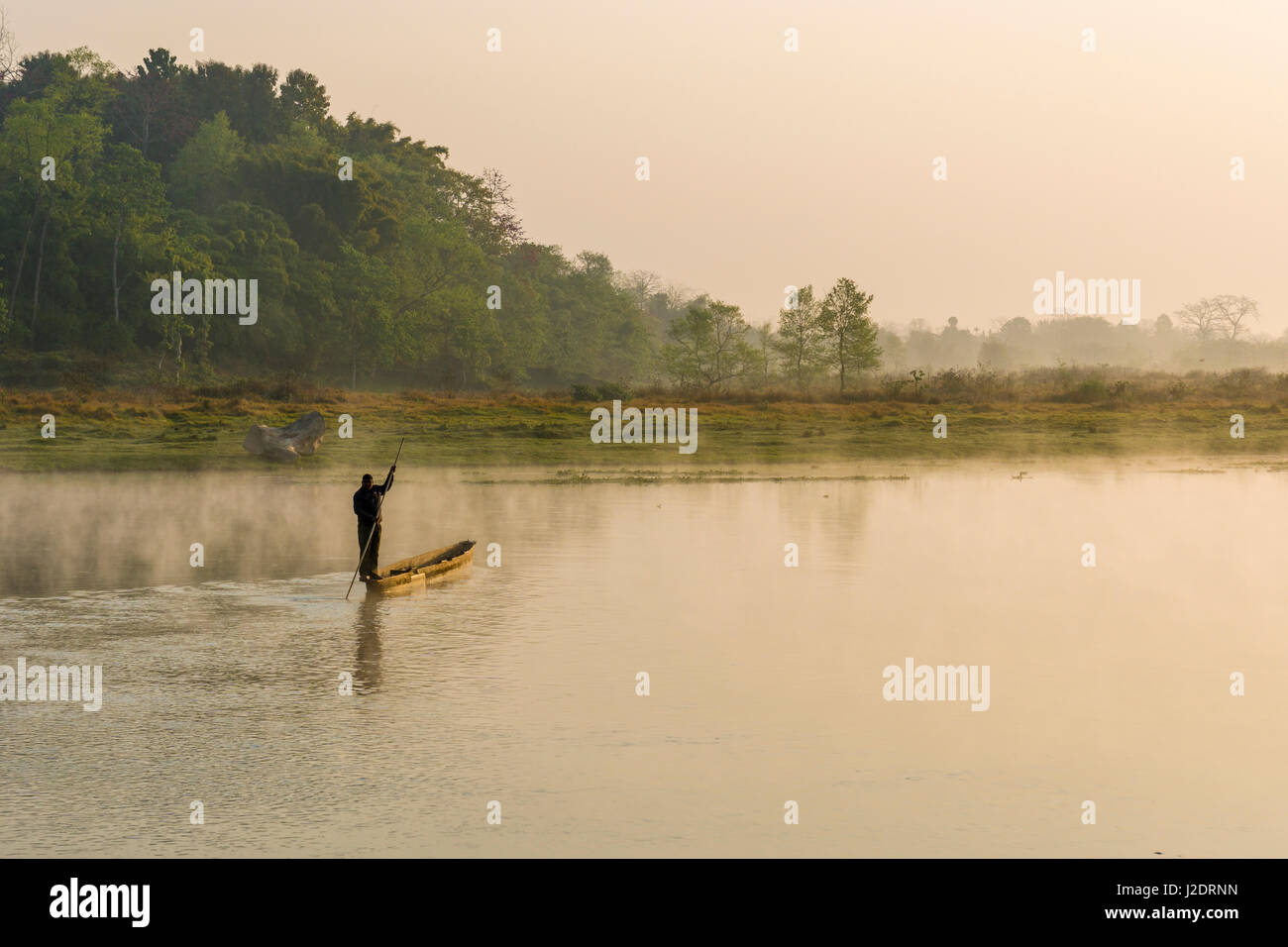 Un uomo attraversa la nebbia fiume rapti in Chitwan il parco nazionale di mattina in barca Foto Stock