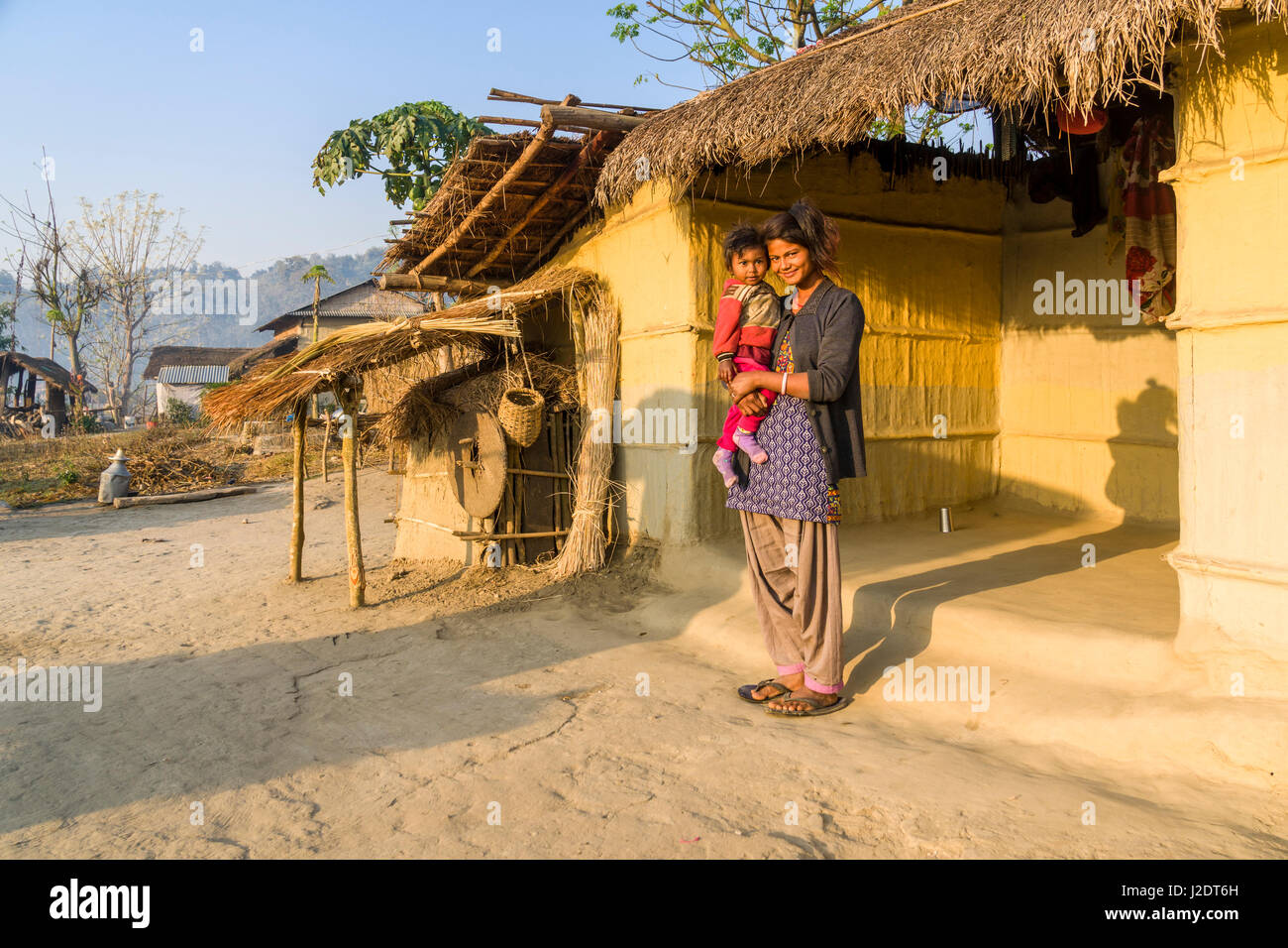 Una giovane donna, portando il suo bambino, sono in piedi di fronte ad un tipico agriturismo nel villaggio pandavnagar in Chitwan il parco nazionale Foto Stock