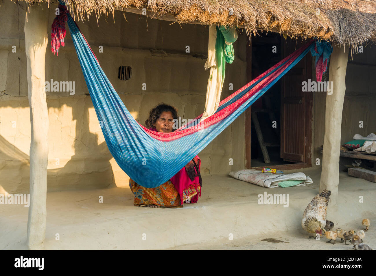 Una donna del suo bambino dorme in un amaca è seduto di fronte ad un tipico agriturismo nel villaggio pandavnagar in Chitwan il parco nazionale Foto Stock