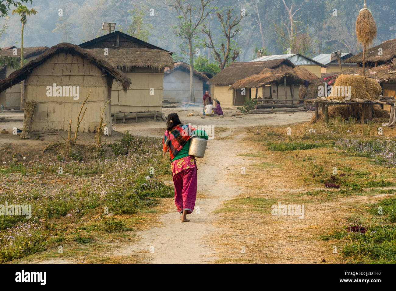 Una donna sta camminando verso le tipiche case coloniche nel villaggio pandavnagar in Chitwan il parco nazionale Foto Stock
