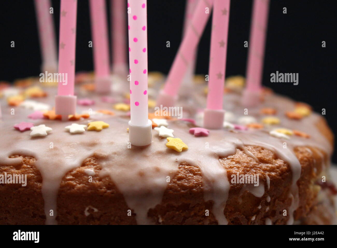 Vista ravvicinata di una celebrazione torta, con glassa, centinaia e migliaia di decorazione, e candele rosa su sfondo nero Foto Stock