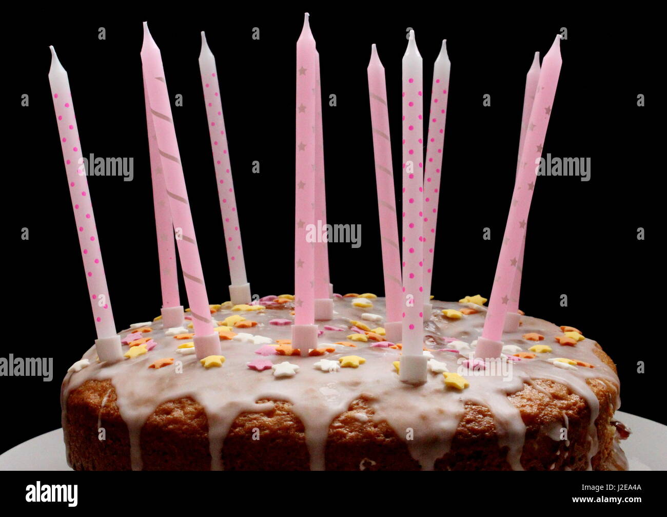 Una celebrazione torta, con glassa, centinaia e migliaia di decorazione, e candele rosa su sfondo nero Foto Stock