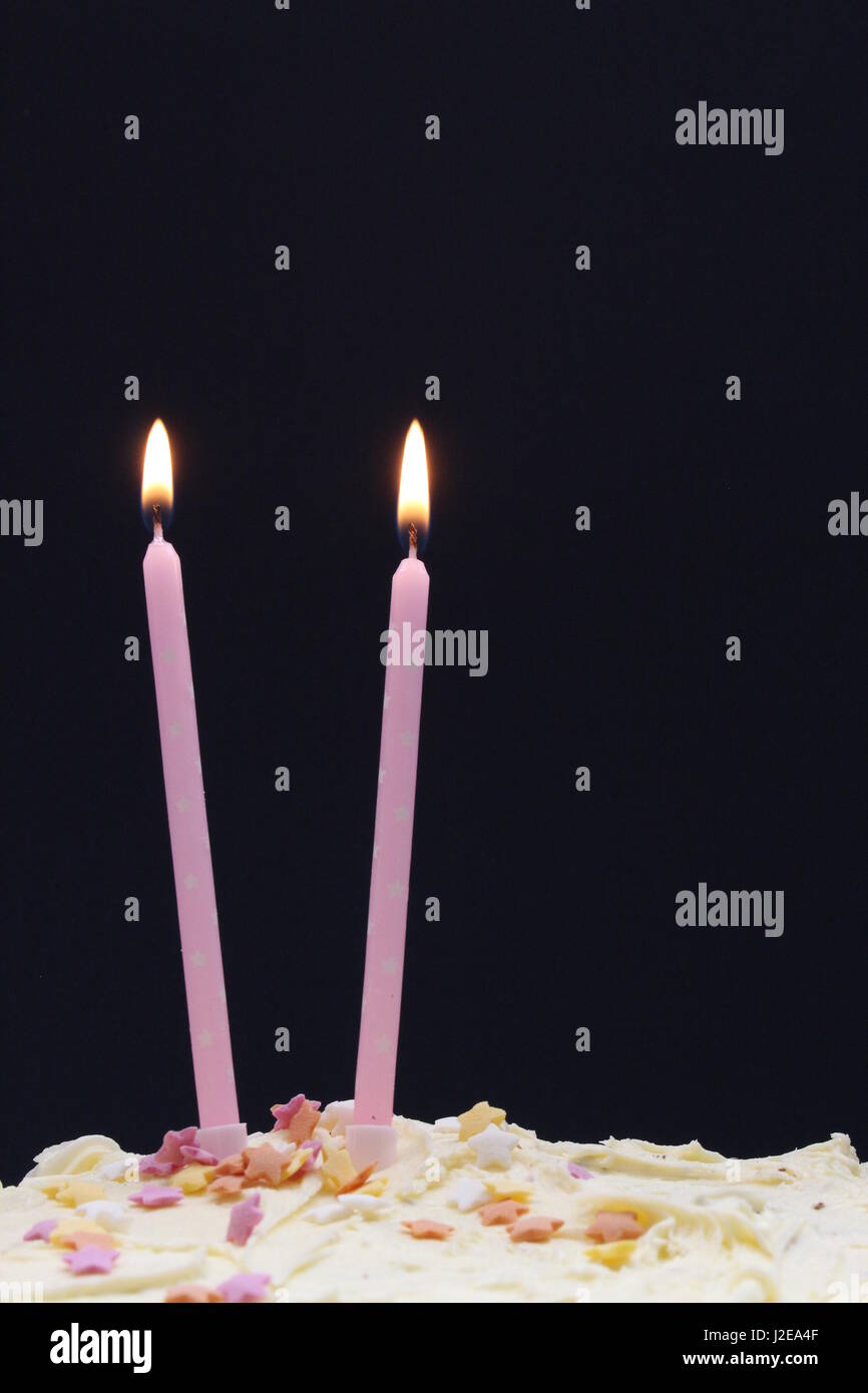 Una celebrazione torta, con glassa, centinaia e migliaia di decorazione, e rosa candele, su uno sfondo nero. Composizione verticale Foto Stock