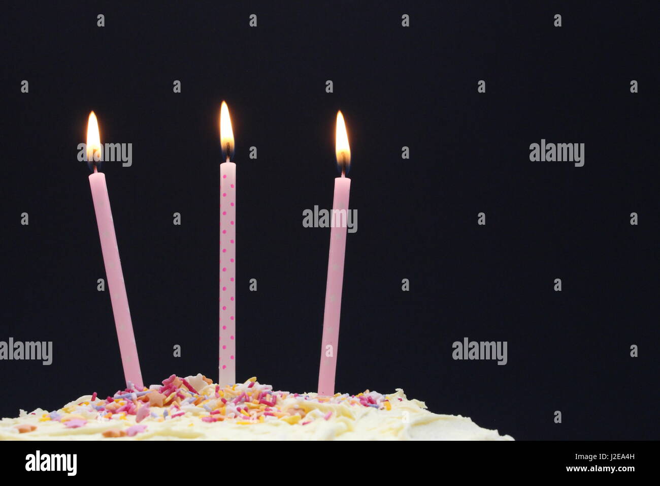 Una celebrazione torta, con glassa, centinaia e migliaia di decorazione, e candele rosa su sfondo nero Foto Stock