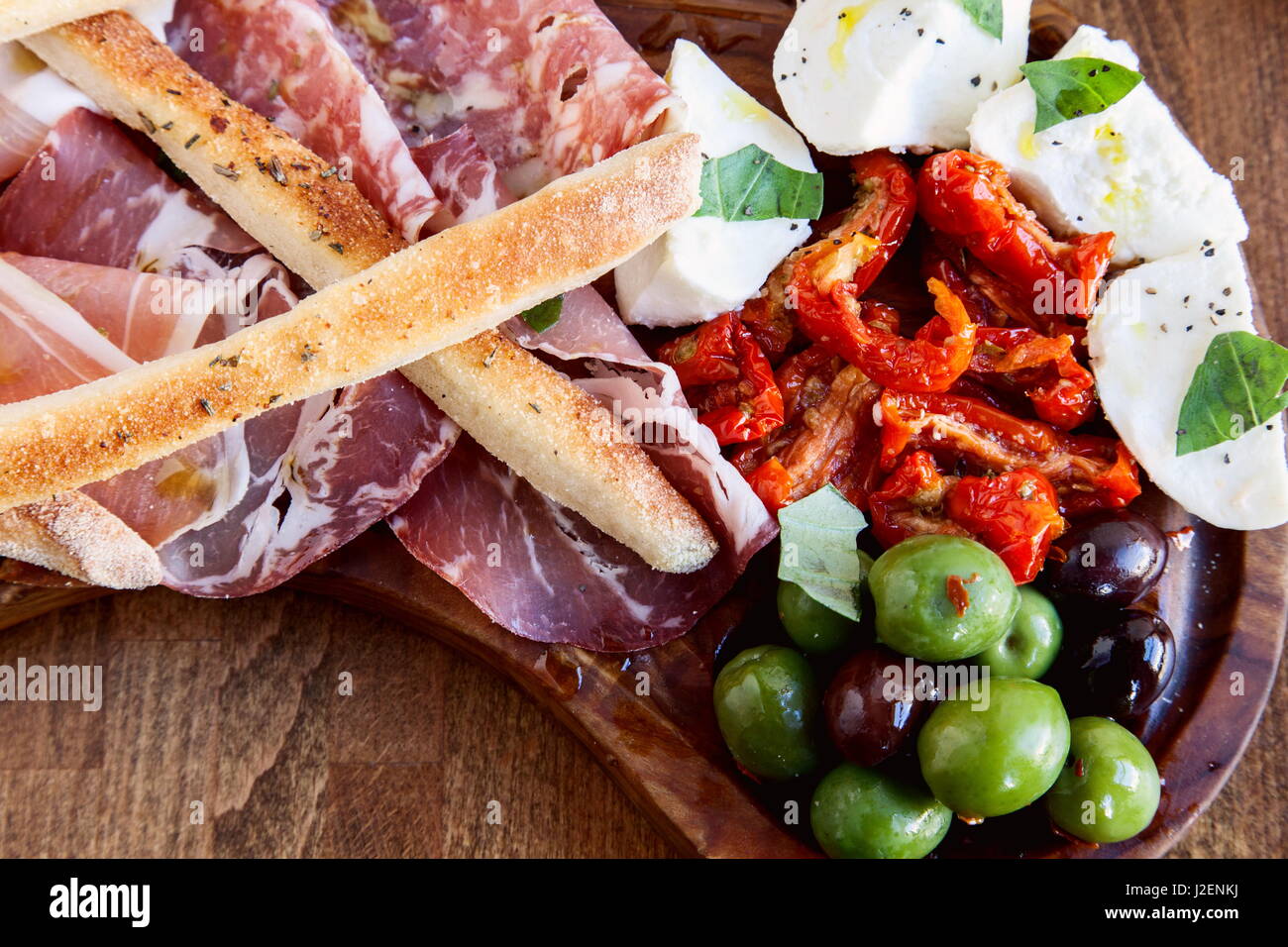 Un piatto di antipasti di salumi, olive, mozzarella di bufala, pomodori secchi e i grissini su una tavola di legno Foto Stock