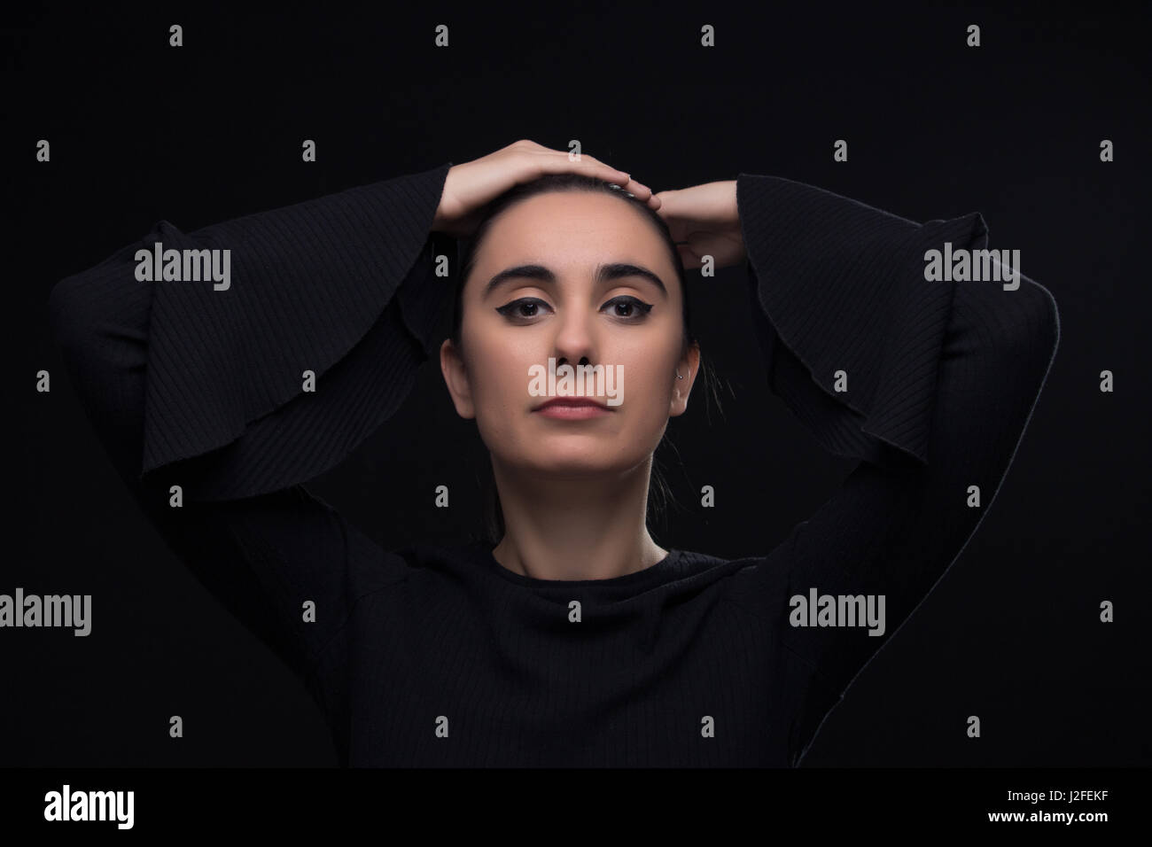 Una giovane donna adulta, vestiti di nero faccia di testa, sfondo nero in studio. Foto Stock