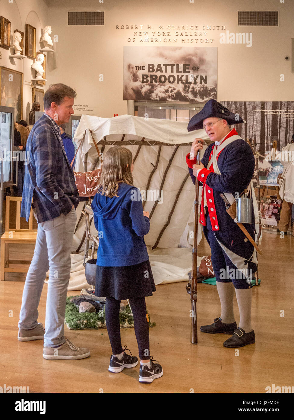 Indossare l'uniforme di un soldato continentale durante la Rivoluzione Americana, un docente presso la New York Historical Society museum di New York City spiega una mostra sul 1776 Battaglia di Brooklyn a un padre e figlia. Nota segno e tenda in background. Foto Stock