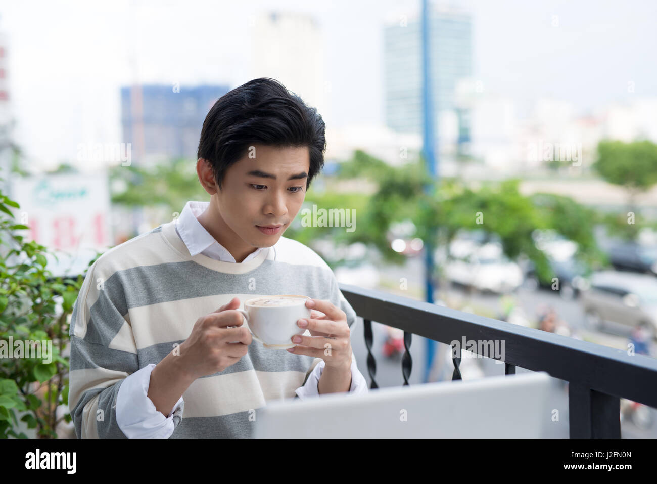 Bello asian giovane uomo che lavora sul computer portatile e sorridere mentre godendo di caffè nella caffetteria Foto Stock