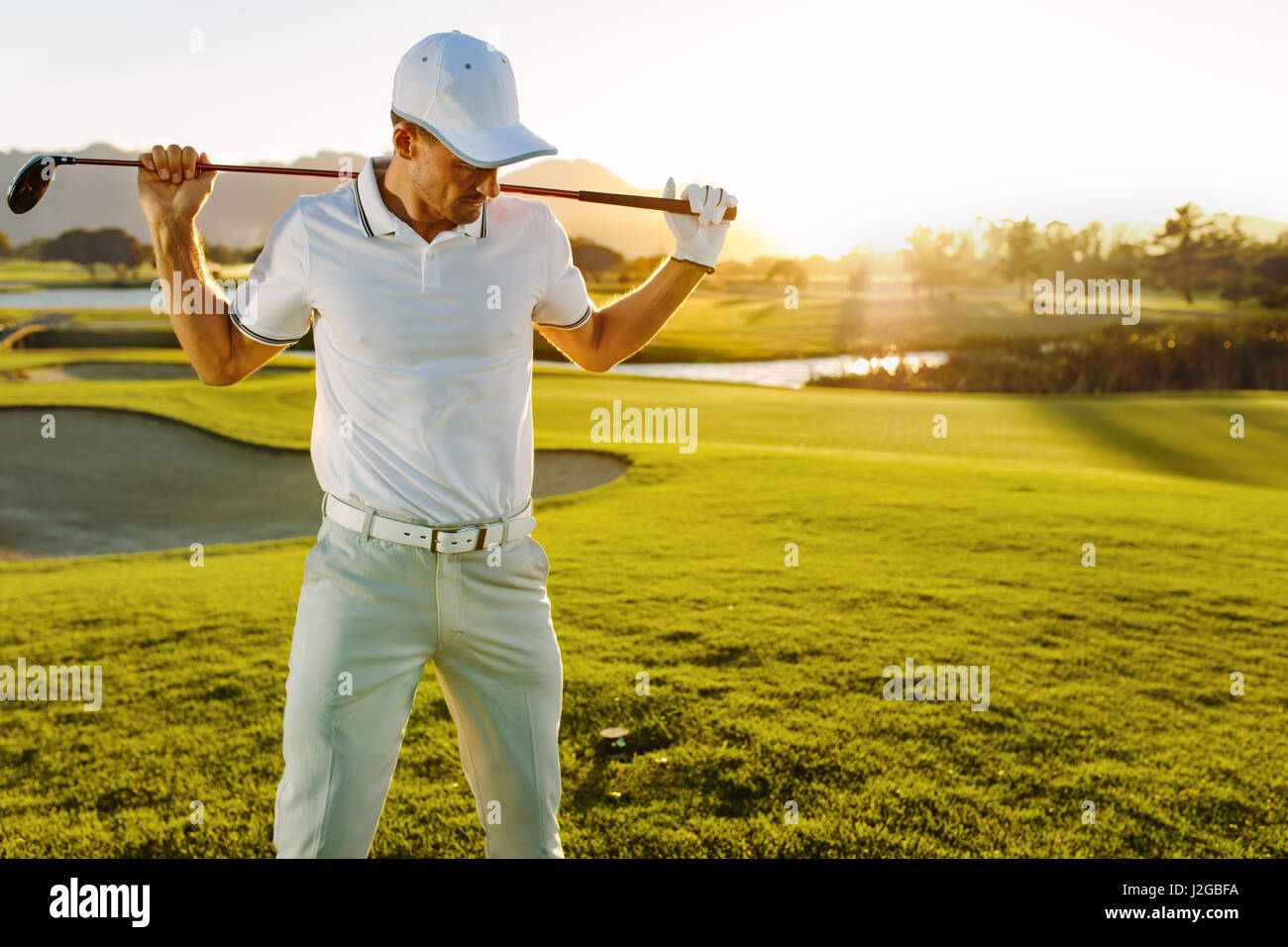 Colpo di golfista maschio con golf club in corso su un giorno d'estate. Giovane uomo tenendo un golf club e guardando verso il basso. Foto Stock