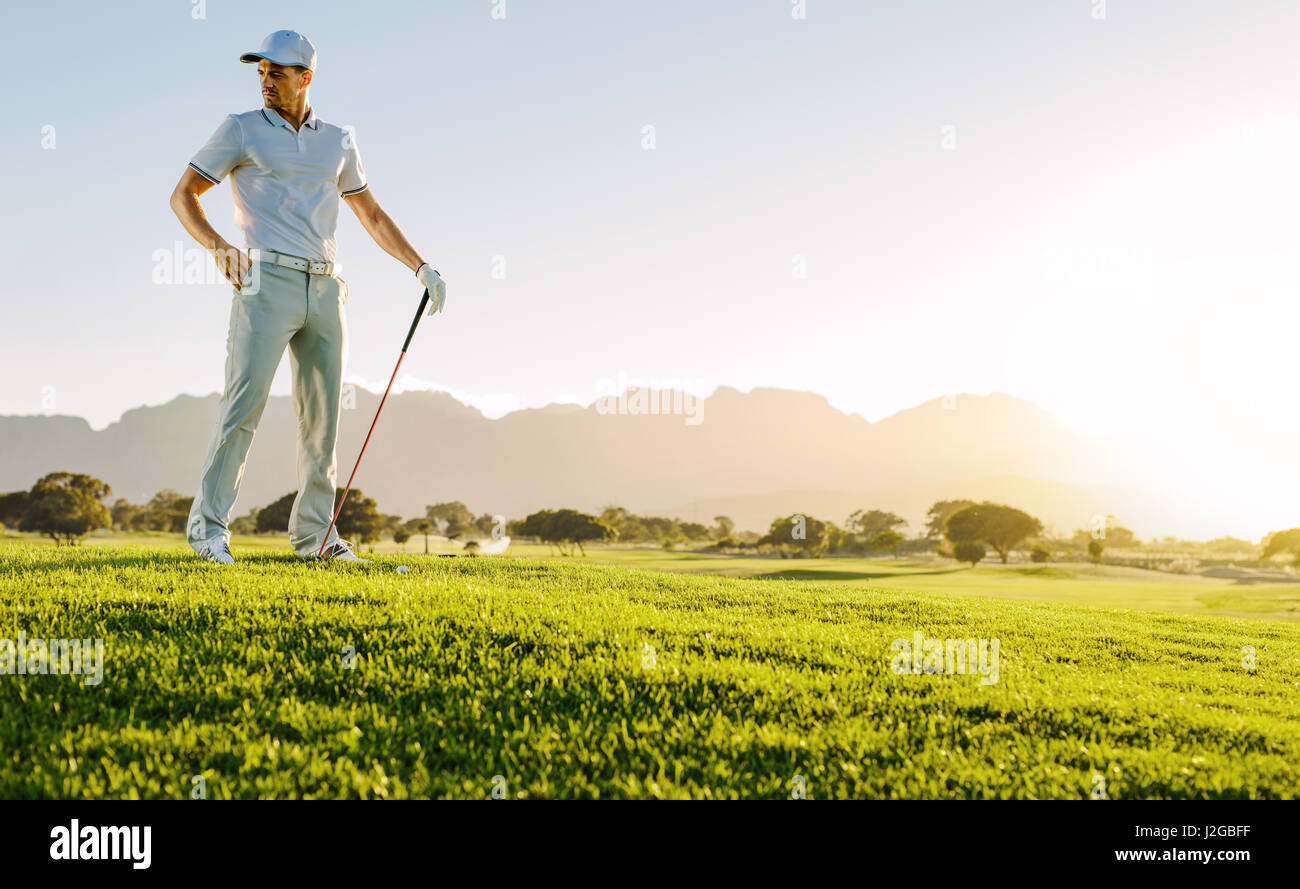 Per tutta la lunghezza della giovane maschio golfista in piedi sul campo da golf su un giorno d'estate. Ritratto di giovane uomo con bastone da golf sul campo. Foto Stock