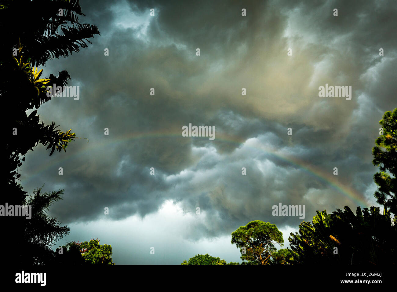 Nuvole temporalesche approccio in questa fotografia mentre un arcobaleno è illuminato dai raggi solari al tramonto. Foto Stock