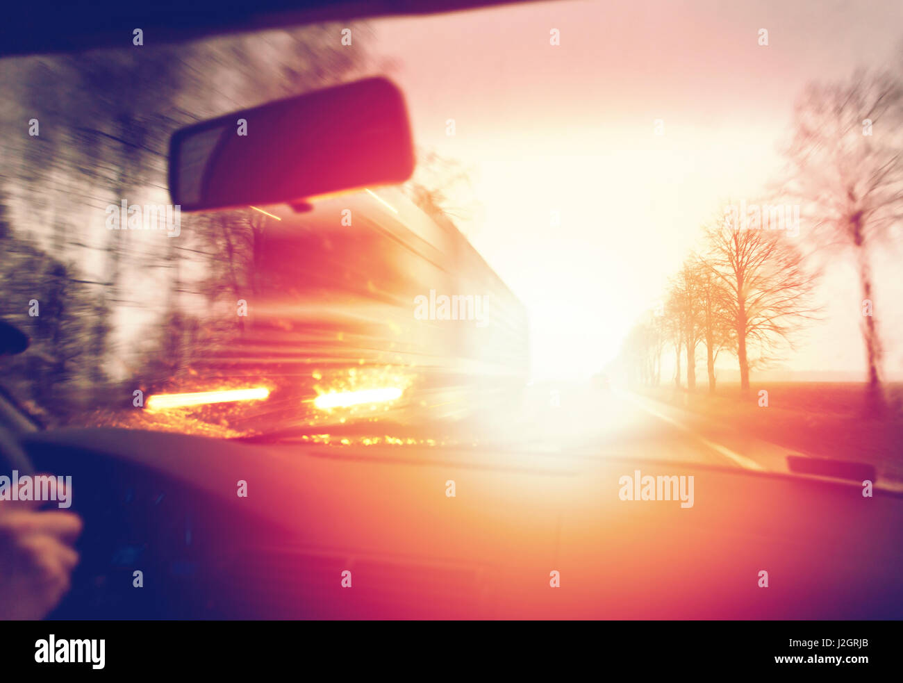 Alla guida di una vettura in mattinata contro sunrise, passando un carrello Foto Stock