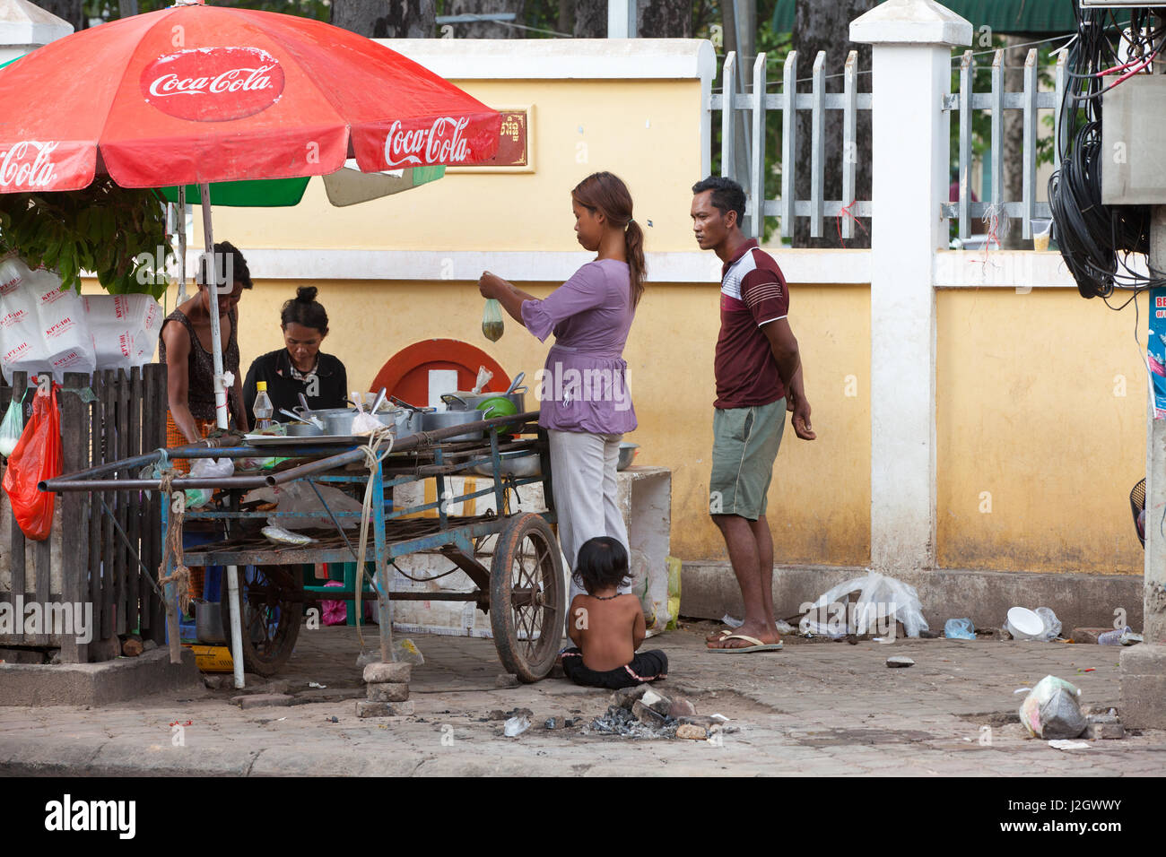 SIEM REAP, Cambogia - 6 Luglio: bambino seduto su un pavimento sporco mentre i suoi genitori che acquistano prodotti alimentari dal cibo in stallo sulla strada di Siem Reap il 6 luglio 2 Foto Stock