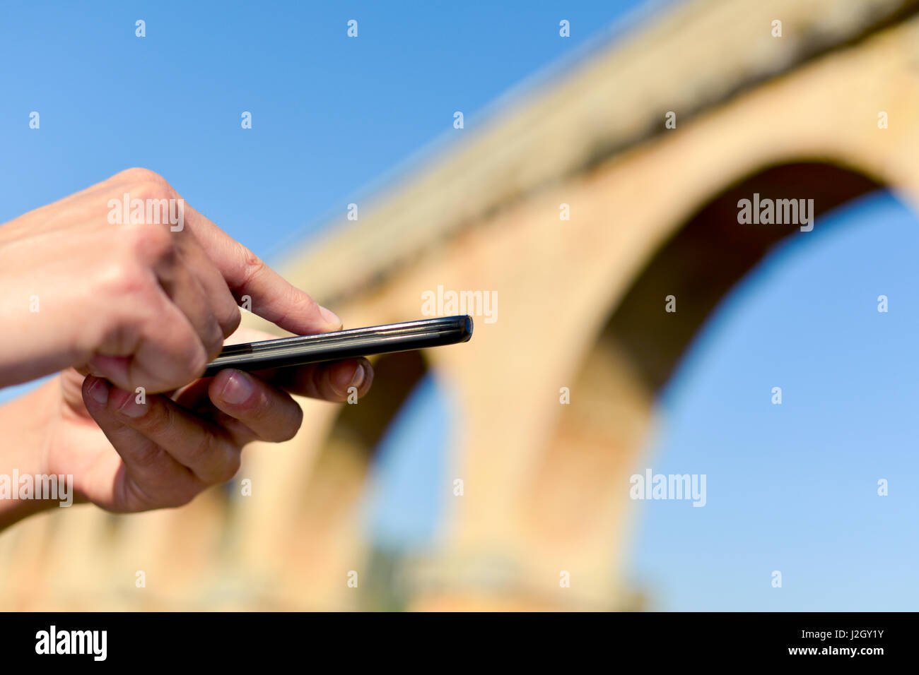 Primo piano di un giovane uomo caucasico utilizzando uno smartphone all'aperto di fronte alcuni antichi resti architettonici Foto Stock