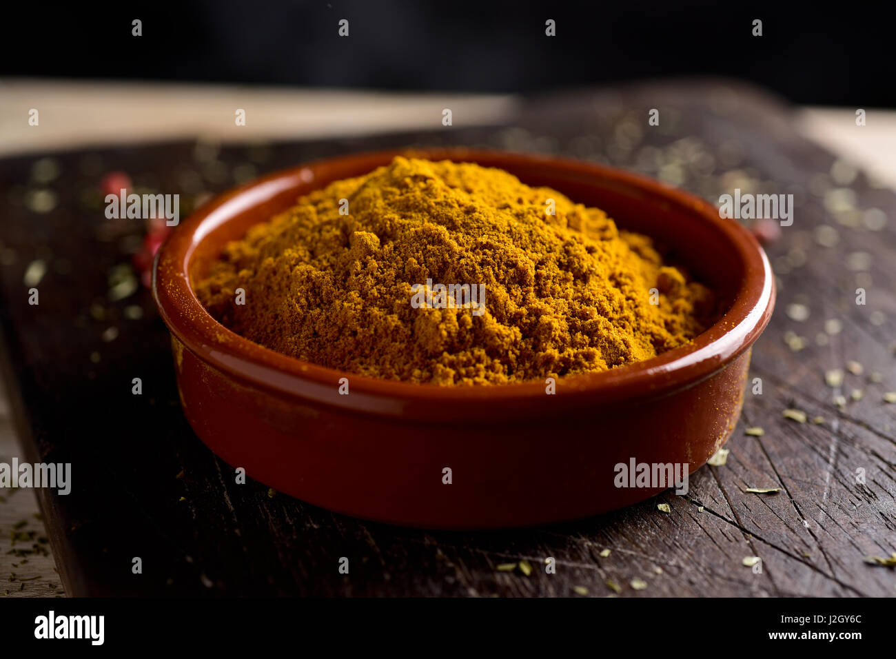 Primo piano di un recipiente di terracotta piena di curry in polvere, su un rustico tagliere di legno, su un tavolo Foto Stock