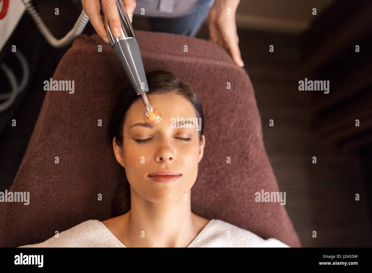 Donna con faccia microcurrent massaggiatore in spa Foto Stock