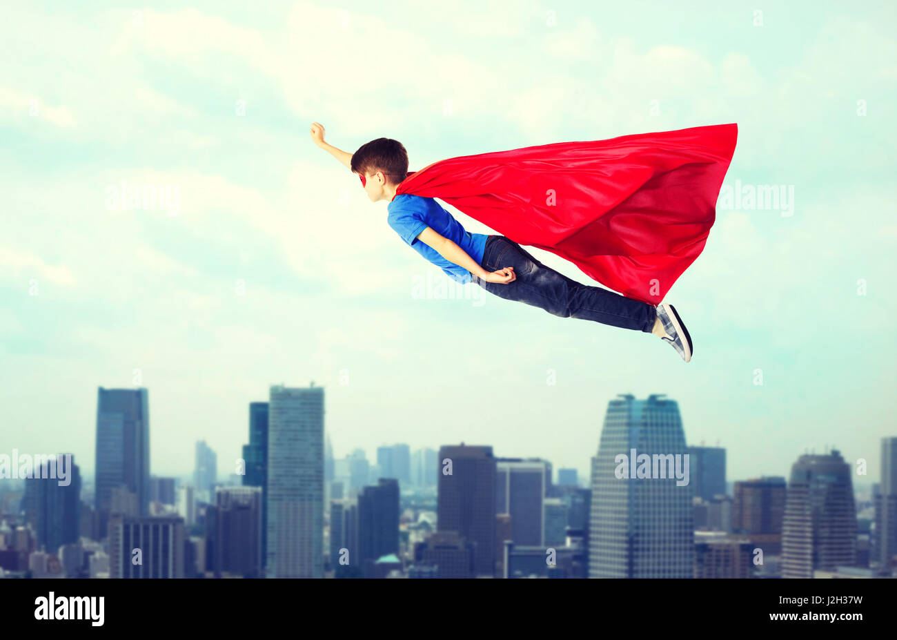 Ragazzo in rosso superhero cape e maschera e volare in aria Foto Stock