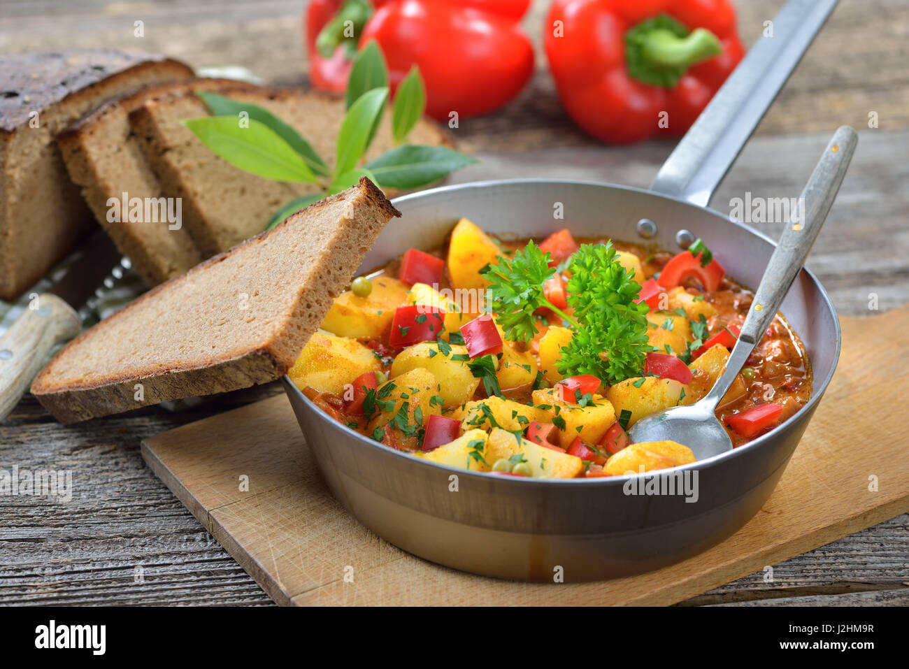 Hot vegetariano gulasch di patate servita in una padella di ferro con deliziosi scuro agriturismo cotto il pane su un vecchio tavolo di legno, una tirolese specialità di montagna Foto Stock