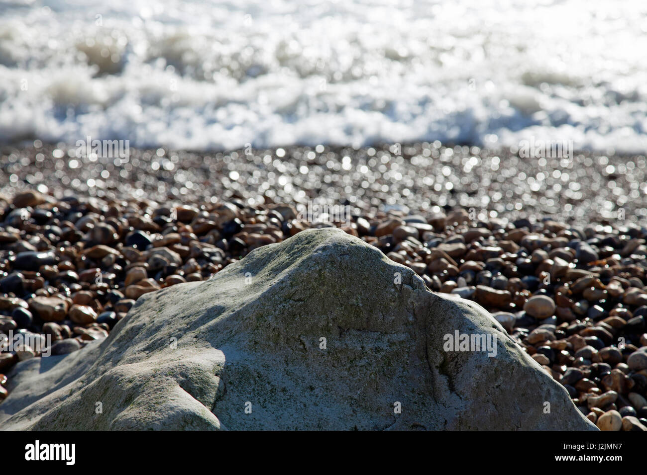Wintery di luce che cade su una roccia solitaria su una spiaggia di ciottoli con il mare oltre Foto Stock