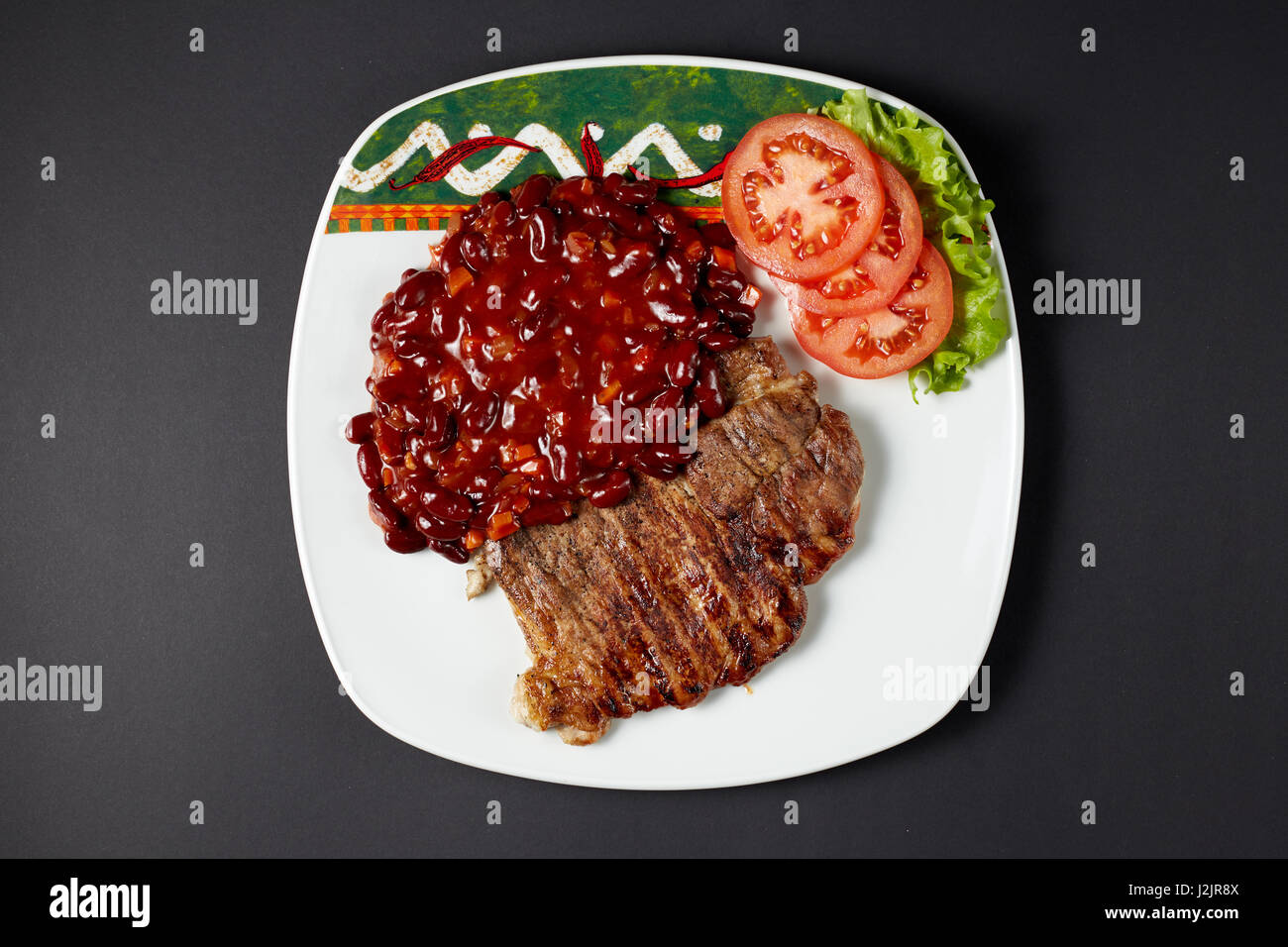 Bistecca di carne di maiale con fagioli. Cibo messicano. Cucina messicana. Studio shot sul buio o sfondo nero. Foto Stock