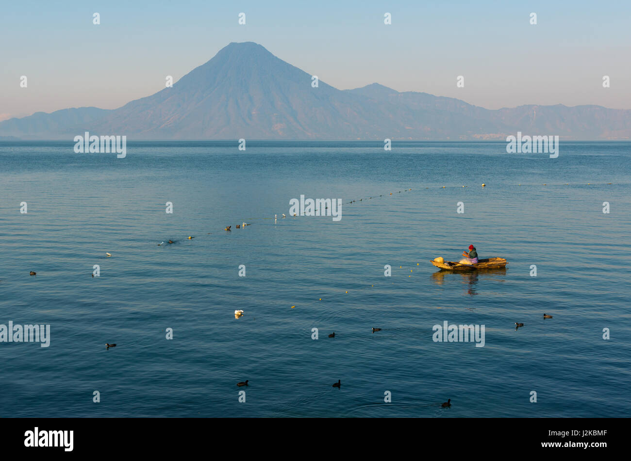 Pescatore nella sua barca controllare le sue reti nelle acque blu del lago Atitlan con un vulcano sullo sfondo vicino a Panajachel in Guatemala. Foto Stock