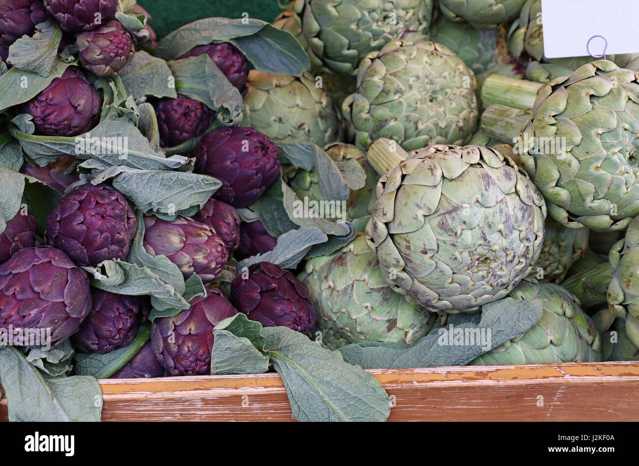 Verde e viola freschi carciofi in scatola di legno sul mercato al dettaglio, display a basso angolo di visione Foto Stock