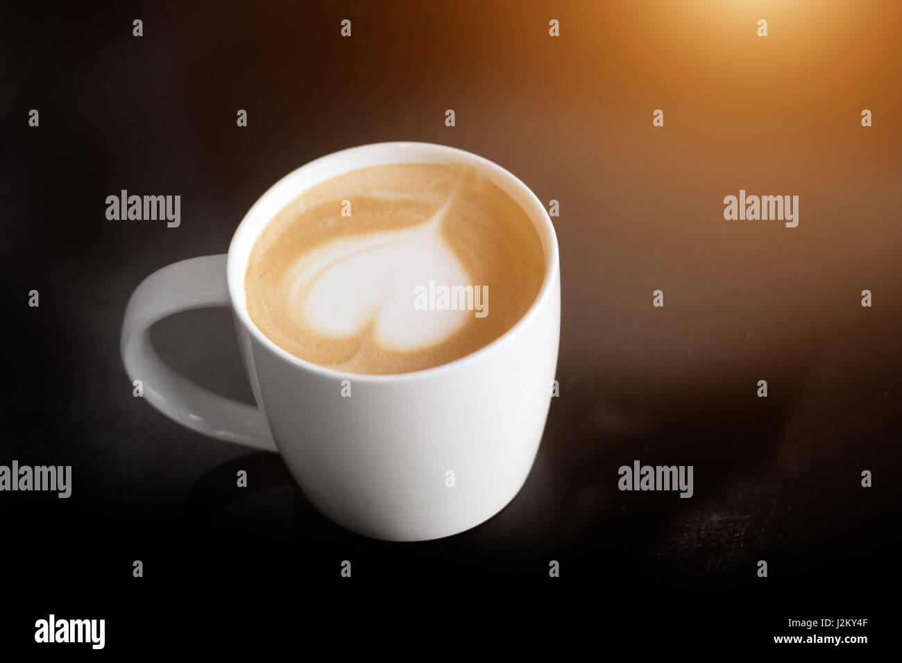 Latte Art come forma di cuore in tazza di caffè con tenere in mano la tazza per il caldo in uno sfondo scuro Foto Stock