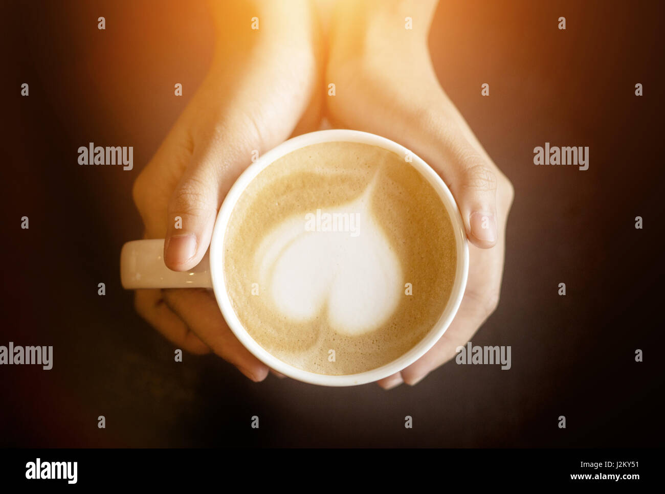 Latte Art come forma di cuore in tazza di caffè con tenere in mano la tazza per il caldo in uno sfondo scuro Foto Stock