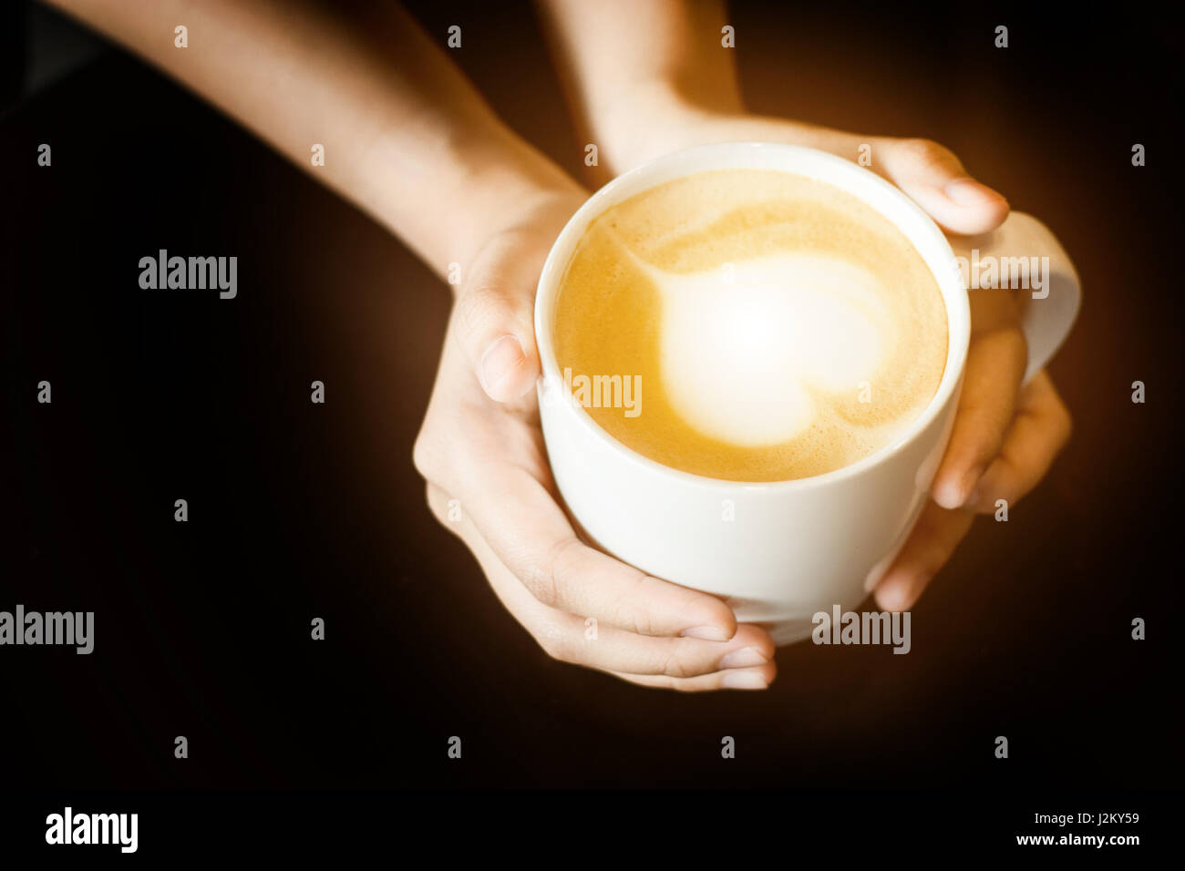 Latte Art come forma di cuore in tazza di caffè con tenere in mano la tazza per il caldo in uno sfondo scuro Foto Stock