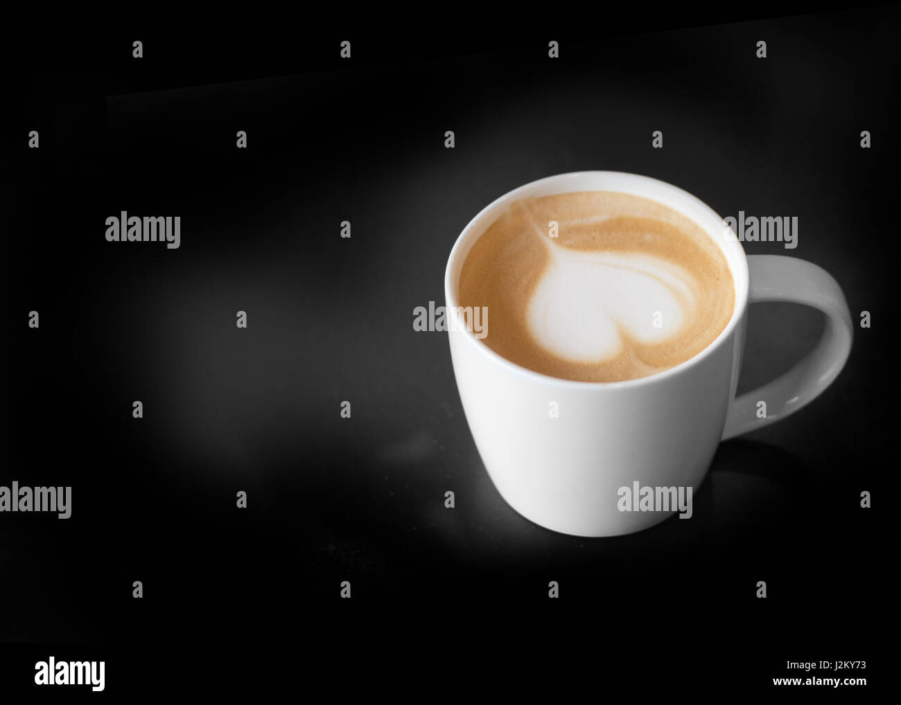 Latte Art come forma di cuore in tazza di caffè con tenere in mano la tazza per il caldo in uno sfondo scuro Foto Stock