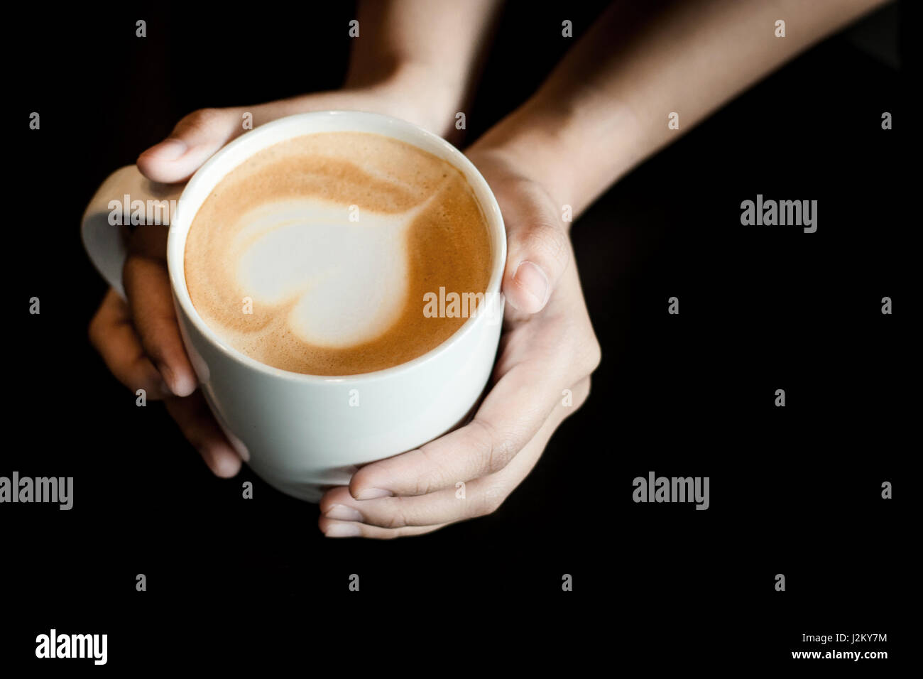 Latte Art come forma di cuore in tazza di caffè con tenere in mano la tazza per il caldo in uno sfondo scuro Foto Stock