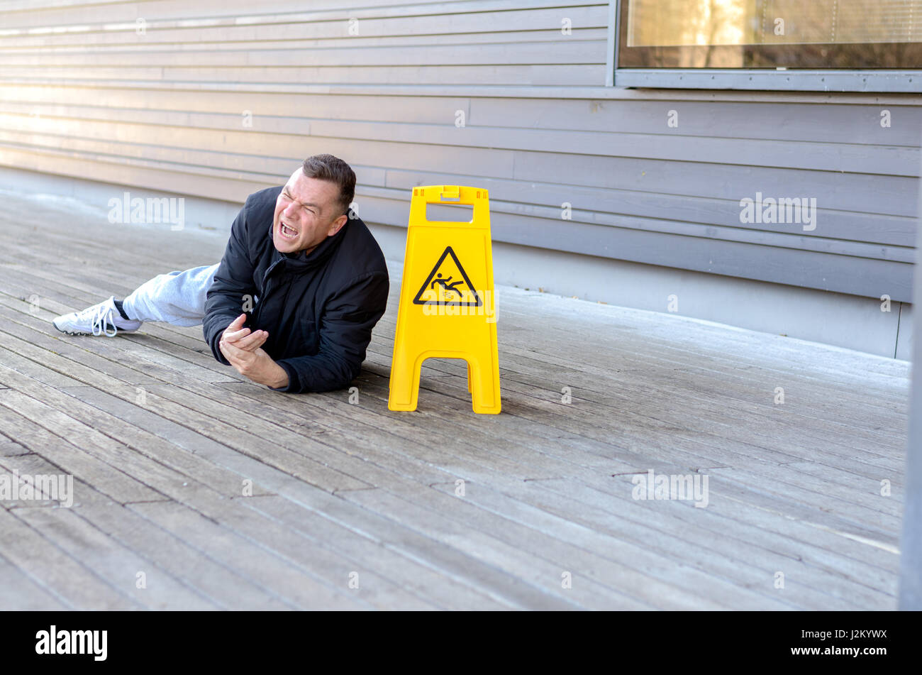Uomo di mezza età prese una caduta su un pavimento scivoloso proprio al fianco di un portatile di simbolo giallo di avvertimento smorfie nel dolore laterale con spazio di copia Foto Stock