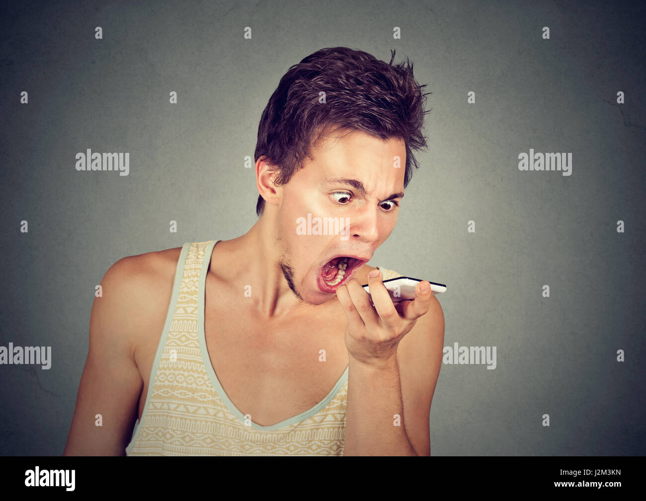 Ritratto iracondo urlando sul telefono cellulare isolato su sfondo grigio. Le emozioni negative sentimenti Foto Stock