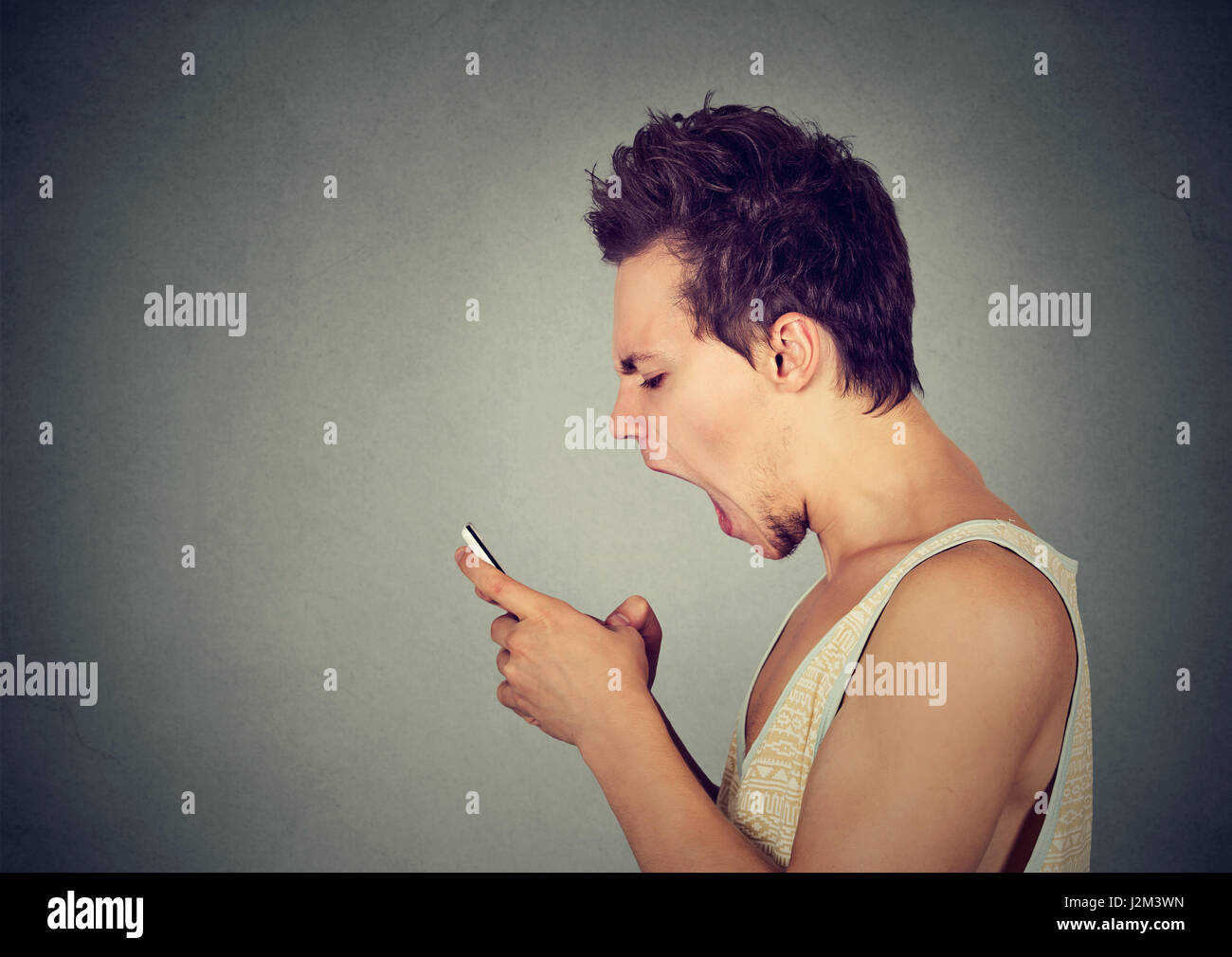 Profilo laterale ritratto iracondo urlando sul telefono cellulare isolato su sfondo grigio. Le emozioni negative faccia l'espressione di sentimenti atteggiamento Foto Stock