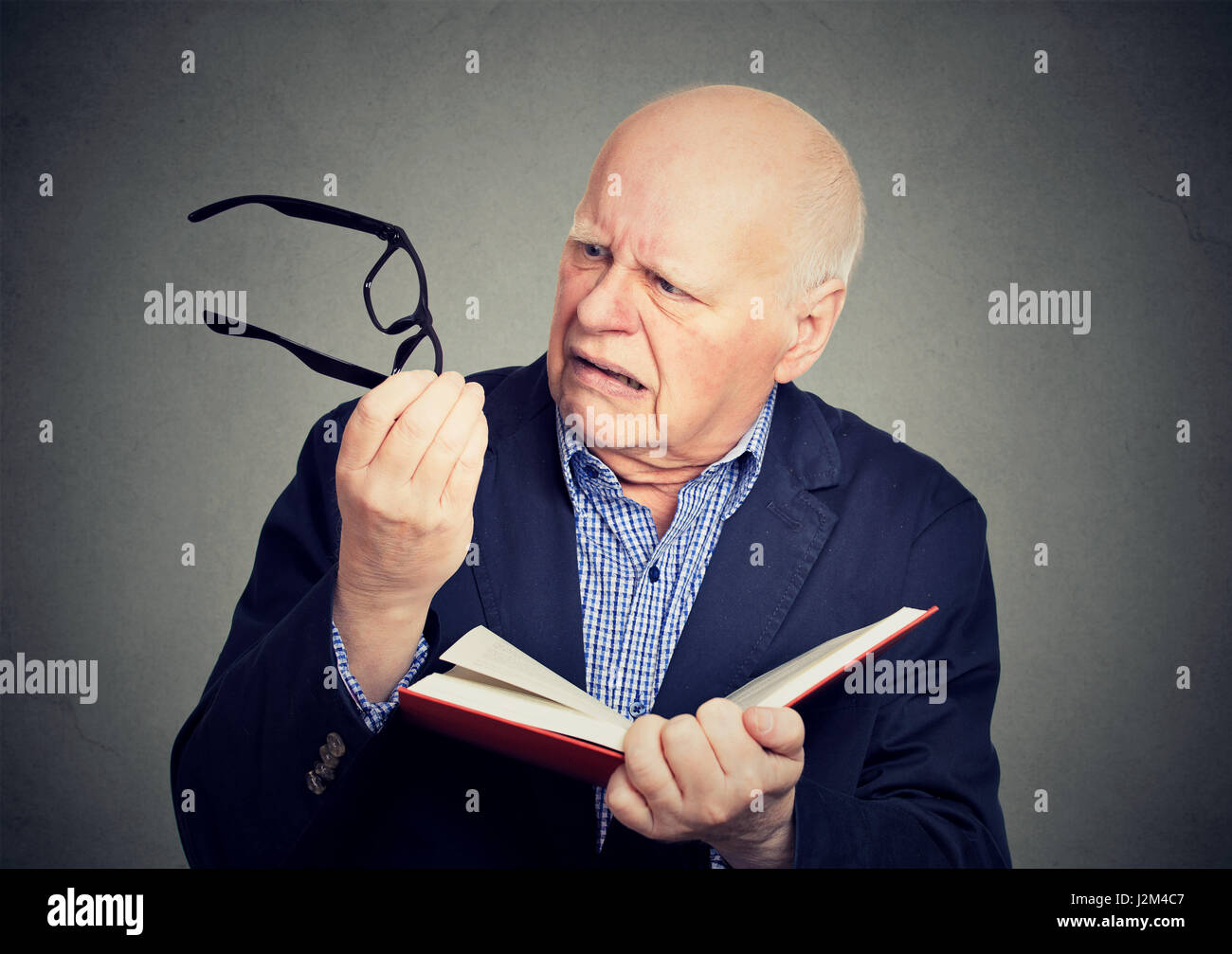 Closeup anziani, uomo maturo azienda prenota, occhiali aventi problemi di vista non in grado di leggere isolato su sfondo grigio. Correlate all'età cambiamenti di salute Foto Stock