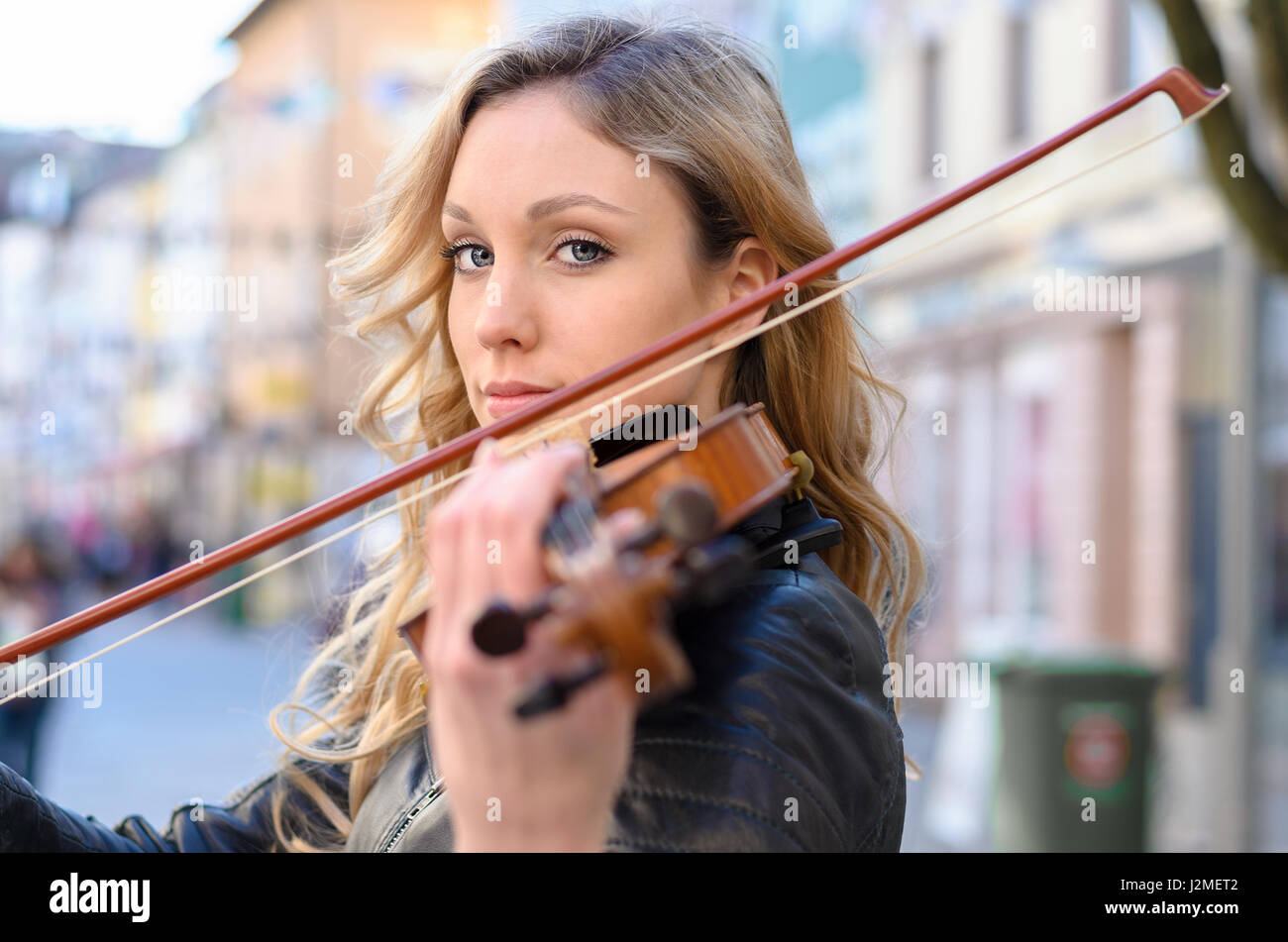 Giovane donna bella violin player guardando la fotocamera su uno strumento sulla sua spalla holding bow. Close-up verticale con edifici in street sfocato Foto Stock