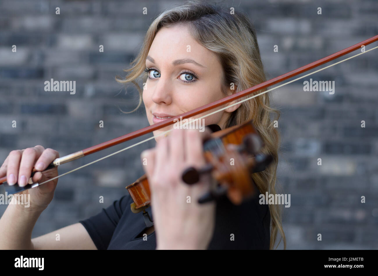 Giovane bella donna ondulata con capelli biondi riproduzione viola, tenendo bow oscillando su uno strumento sulla sua spalla e sorridente, guardando la fotocamera. Parte anteriore Foto Stock