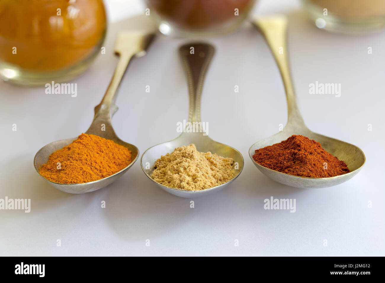 Tre cucchiai di metallo con la curcuma, zenzero e paprika spice, su sfondo bianco, rivolta verso la telecamera con soft-focus barattoli per la parte posteriore. Foto Stock