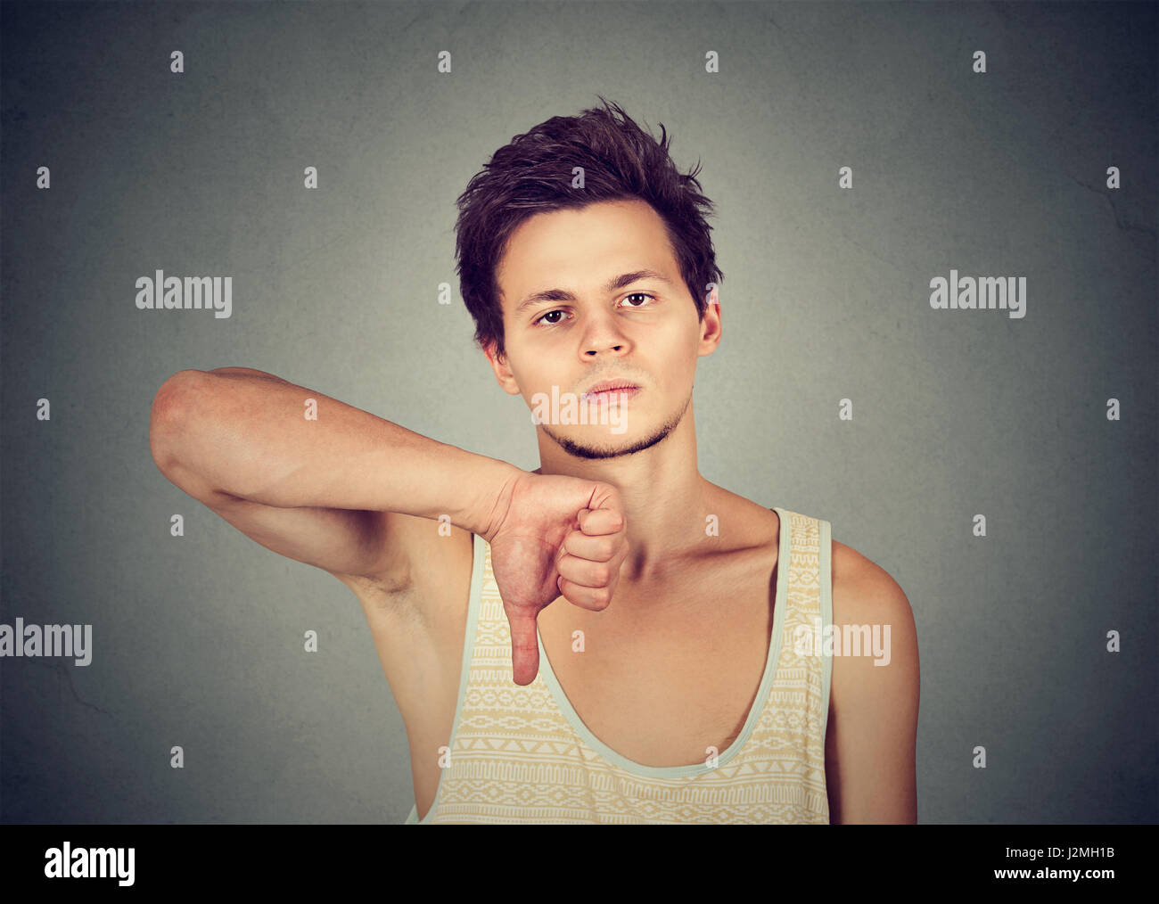 Ritratto di fiducioso giovane uomo guardando la telecamera dando pollice in giù la mano gesto isolato su sfondo grigio Foto Stock