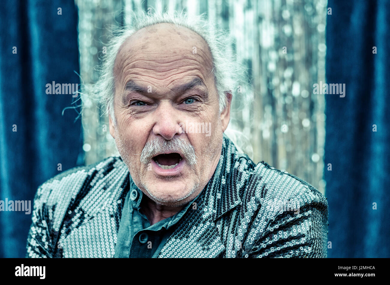 Arrabbiati dai capelli grigi balding man e stridente a urlare contro la fotocamera con un feroce espressione in una testa e spalle visualizza Foto Stock