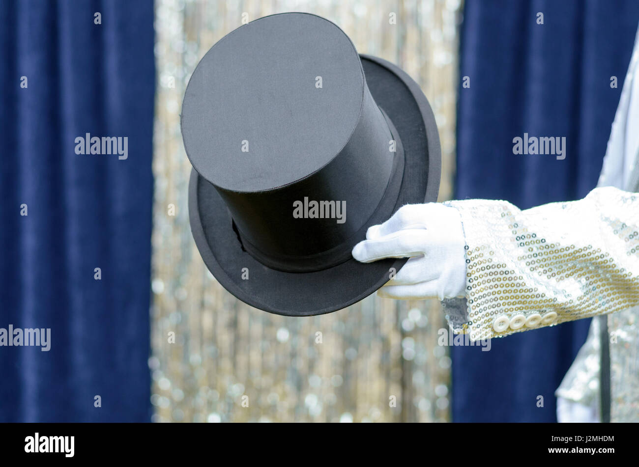 Gentleman o mago tenendo fuori un top hat nella sua mano nella parte anteriore di un azzurro sipario di un palcoscenico con festosa tinsel argento Foto Stock