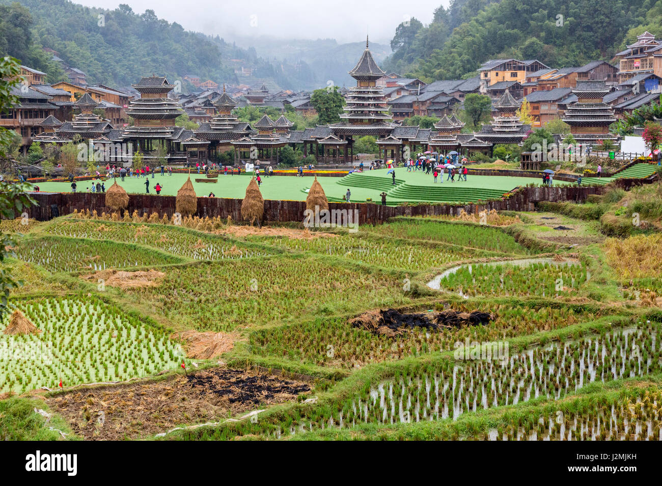 Zhaoxing, Guizhou, Cina, a Dong villaggio di minoranza. Risaie in primo piano, ingresso al villaggio in background. Foto Stock