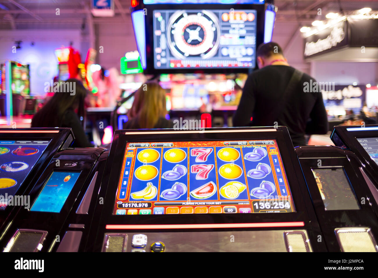 Una slot machine monitor è visto in un casinò con sagome di persone in background. Frutti presso il monitor della slot machine. Foto Stock