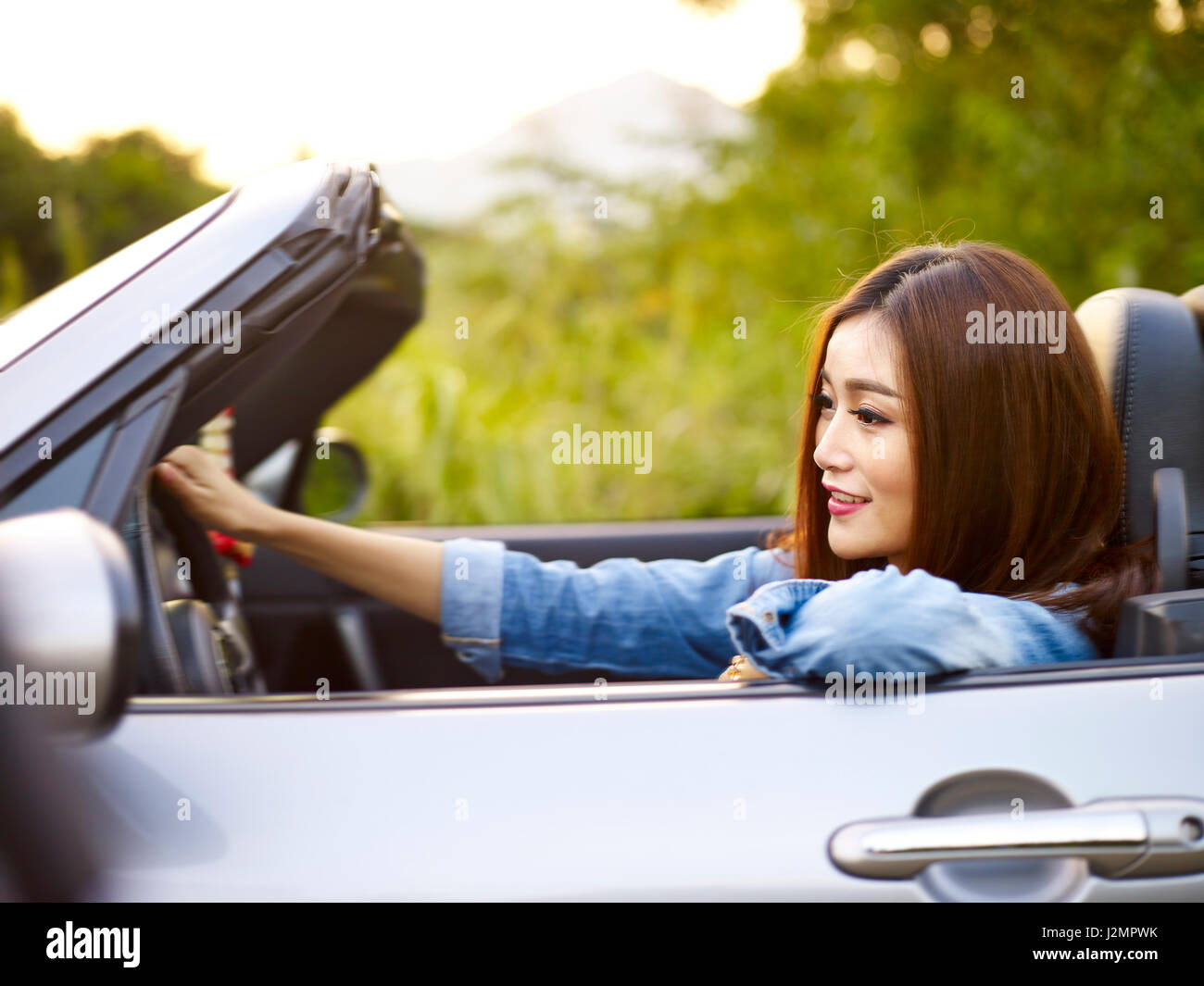 Giovane donna asiatica di equitazione in una cabriolet auto sportive, felice e sorridente. Foto Stock